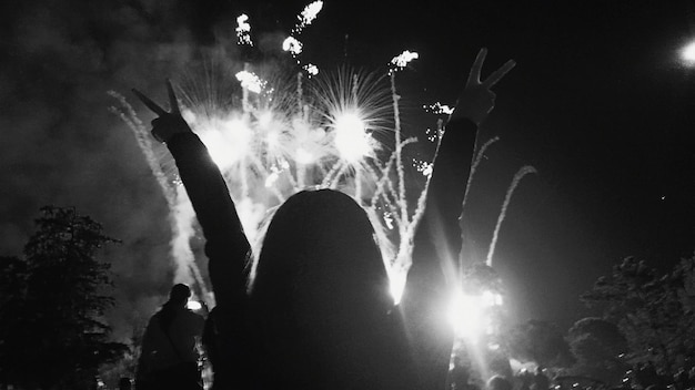 rear view of woman with peace sign against firework display at night