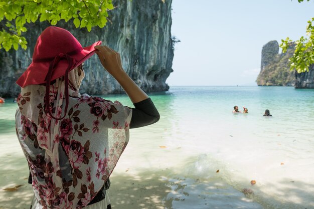 Foto vista posteriore di una donna con un cappello rosso in piedi sulla spiaggia