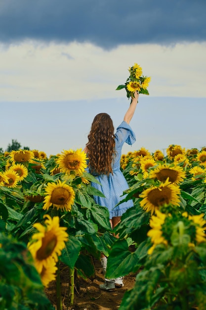 ひまわりの花束を持つ女性の後姿 ひまわりを手に空に手を差し伸べる若い女性