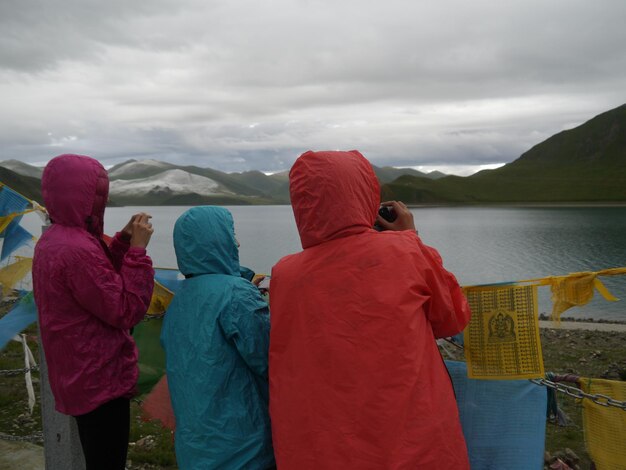 Foto vista posteriore di donne che fotografano lago e montagne contro un cielo nuvoloso