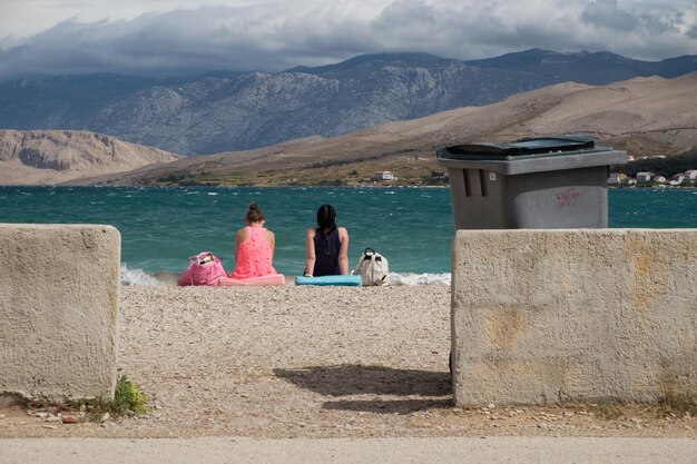 Задний вид женщин, сидящих на пляже на фоне облачного неба