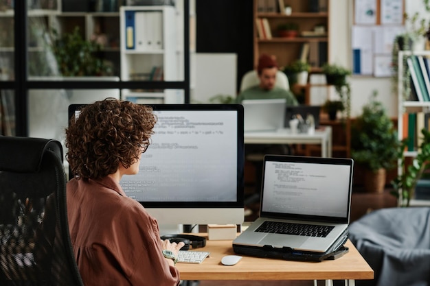 Rear view of young brunette female it specialist in front of computers