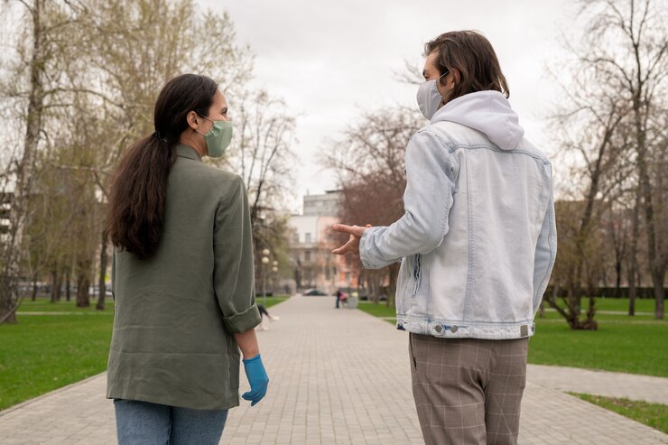 Photo rear view of young contemporary couple in masks and casualwear talking while moving along road in public park