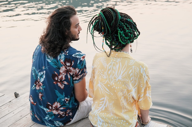 Rear view of young couple talking to each other while sitting on a pier and wetting their feet in the water