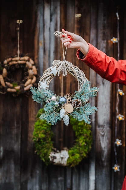 Rear view of young female hipsters decorate home for Christmas at the door outside. Beautiful Christmas tree wreath on old wooden rustic background.