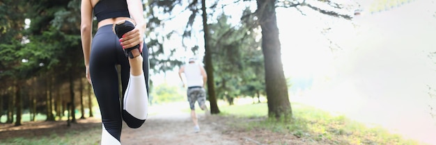 Photo rear view of a young fitness woman stretching leg outdoors in morning in park