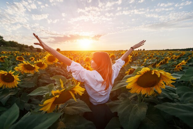 Rear view of a young girl in the middle of a rural area of sunflowers at sunset.