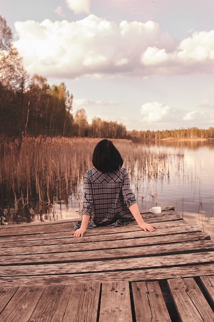 Photo rear view of a young girl sitting on a pier