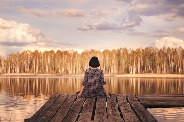 Photo rear view of a young girl sitting on a pier