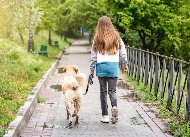 Rear view of young girl walking dog along wet park alley