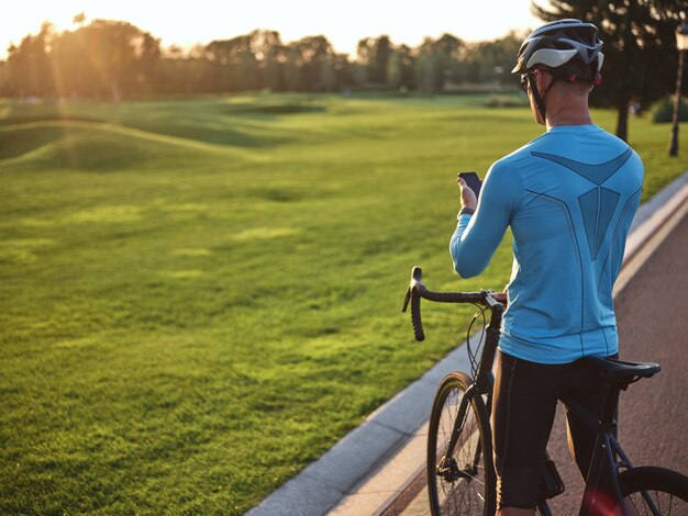 Premium Photo  Rear view of young male cyclist wearing sportswear and  protective helmet holding smartphone standing