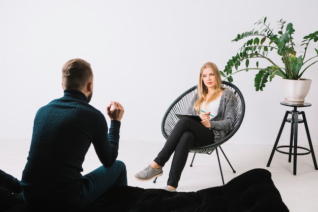 Rear view of a young man discussing her problems with female psychologist sitting on chair in office