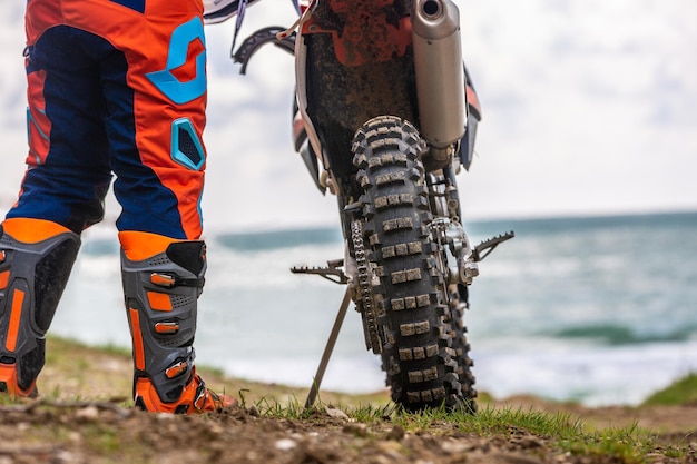 Foto vista posteriore del giovane che guarda in lontananza e in piedi accanto alla motocicletta sulla spiaggia