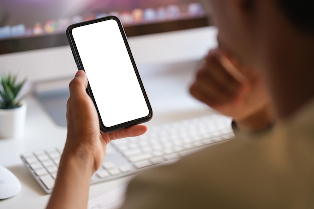 Rear view of young man sitting at his workspace and using smartphone Blank screen for graphics display montage