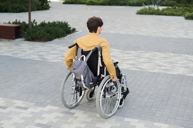 Rear view of young man sitting in wheelchair and spending time outdoors