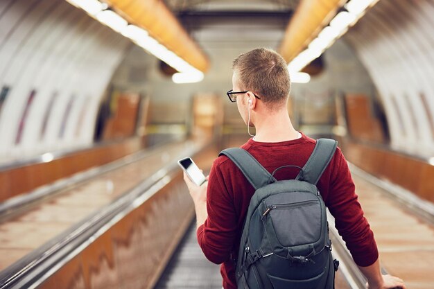 Photo rear view of young man using mobile phone while standing on escalator