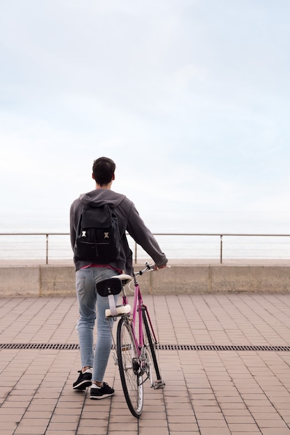 Rear view of a young man walking with a bicycle