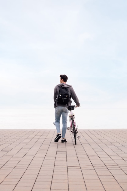 Rear view of a young man walking with a bike