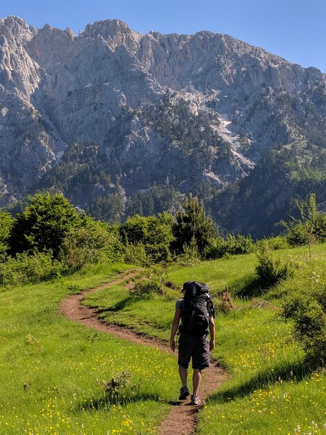 Rear view of young man with backpack walking on trail against mountain during sunny day