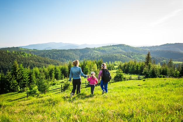 Rear view young mother and two daughters go down the hill overgrown with green grass