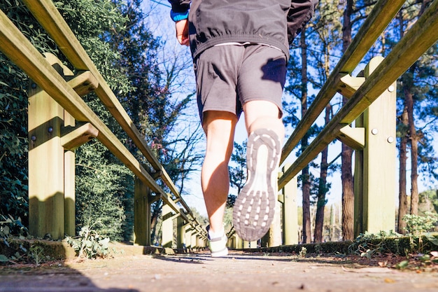 Rear view of young runner running through a wooded park down a wooden walkway in spring or summer sport concept personal care