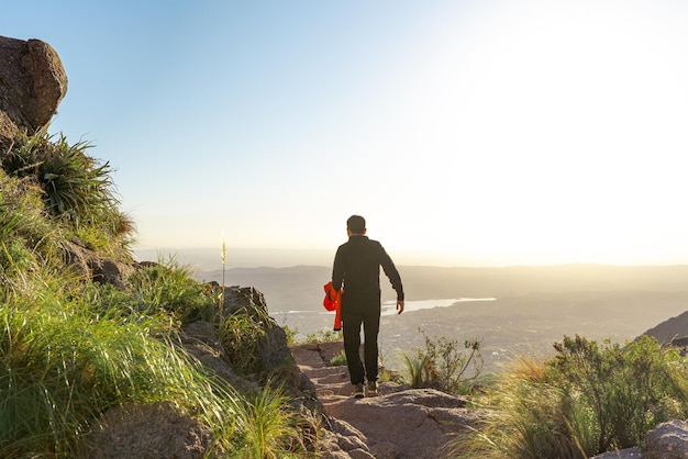 Photo rear view of young tourist man walking on a path in the edge of a mountain at sunset time