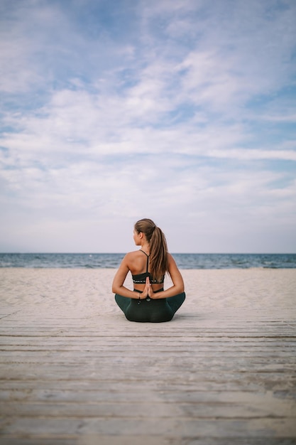 Foto vista posteriore di una giovane donna che fa yoga sulla spiaggia