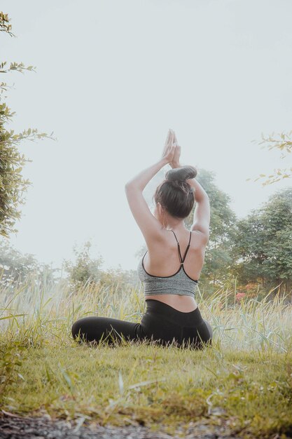 Foto vista posteriore di una giovane donna che fa yoga sul campo contro il cielo