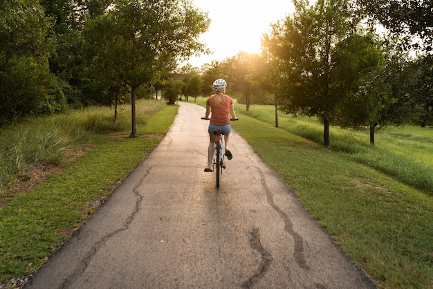 rear view of young woman riding bicycle on road while wearing a helmet
