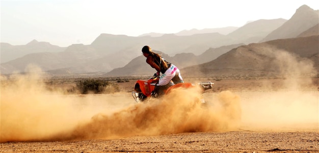 Rear view of young woman riding motorcycle on field against sky