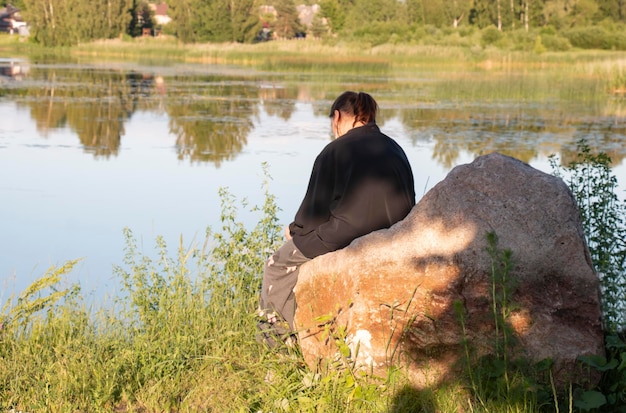 Вид сзади на молодую женщину, сидящую на камне и смотрящую на воду