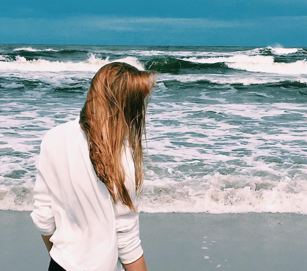 Foto vista posteriore di una giovane donna in piedi sulla spiaggia contro il cielo