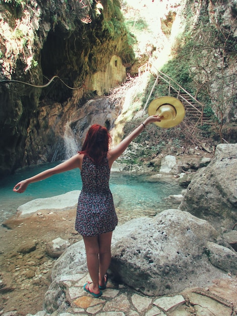 Foto vista posteriore di una giovane donna in piedi su una roccia nella foresta