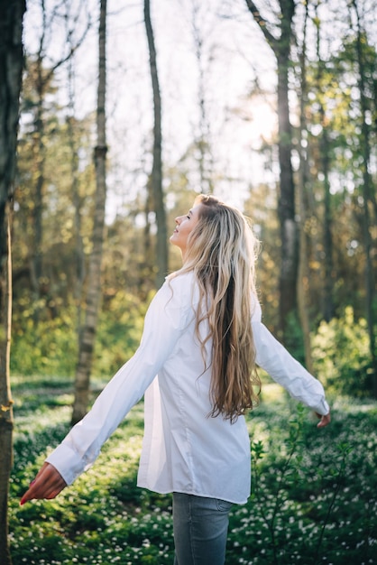 Rear view of young woman standing with open arms enjoying fresh air in spring forest