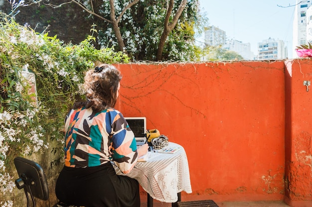 Rear view young woman on the terrace of her house working sitting at a table with her laptop