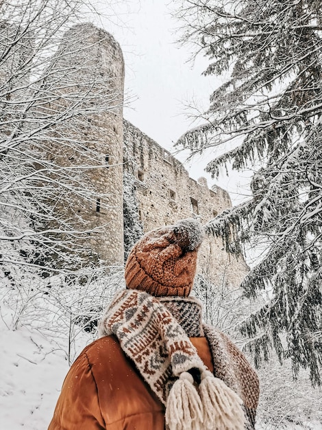 Rear view of young woman in winter clothes. Snowing, looking at old castle ruins, outdoors, style.