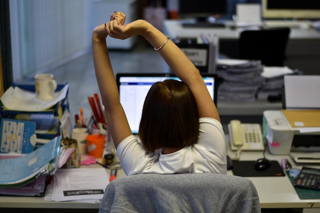 Foto vista posteriore di una giovane donna con le braccia alzate seduta su una sedia in ufficio