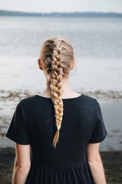 Vista posteriore di una giovane donna con i capelli intrecciati in piedi sulla spiaggia
