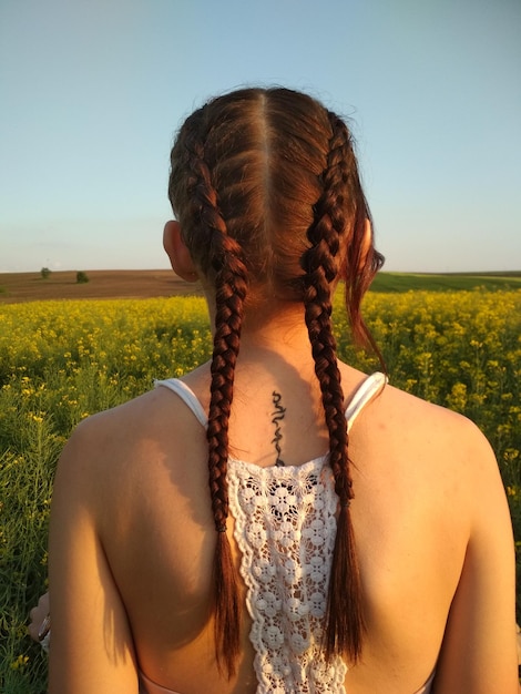 Rear view of young woman with braided hair standing on field against sky