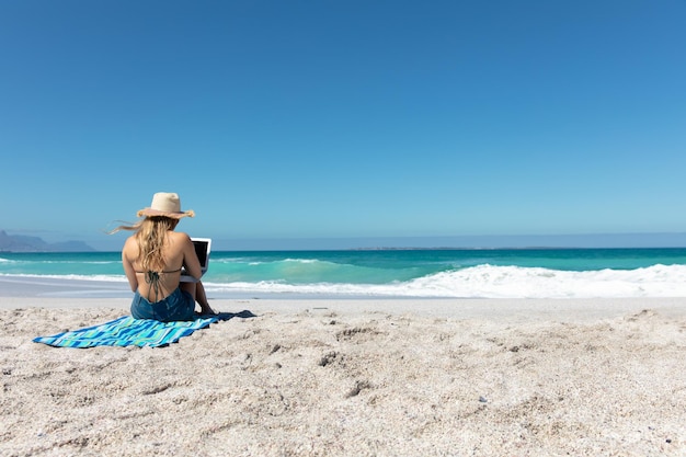 Rear view young woman with computer at the beach