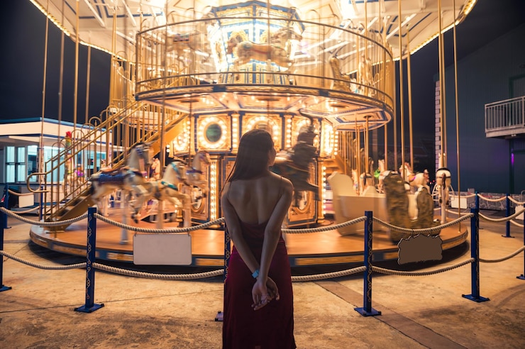 Photo rear of young asian woman in red dress standing in glowing carousel at amusement park
