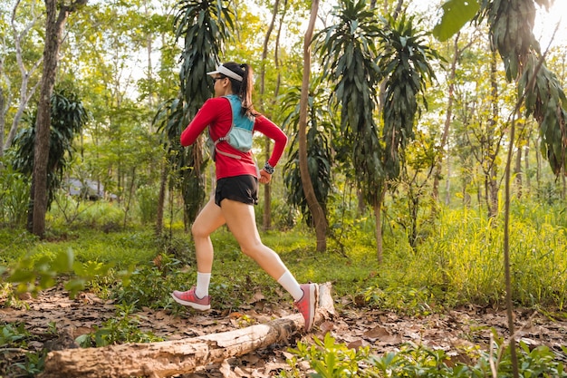 Rearview of adult Asian woman trail runner with running vest practices trail running in the forest