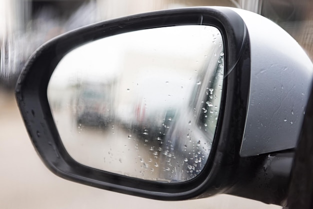 Rearview mirror with raindrops and blurred background in a gray cloudy environment Concept of rain winter sadness dusk darkness fear terror