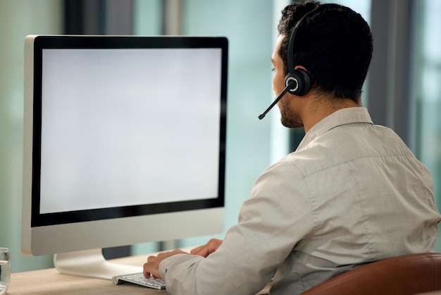 Rearview shot of a young businessman using a headset and computer in a modern office