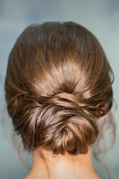 Rearview of young brunette woman with beautiful middle bun hairstyle on gray background.