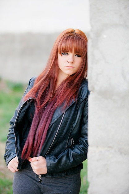 Rebellious teenager girl with red hair leaning on a wall