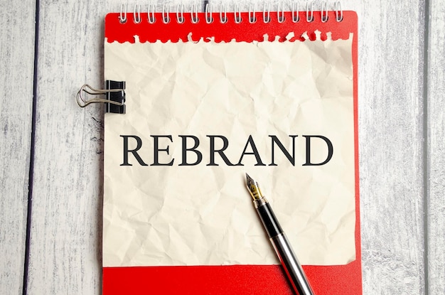 Rebrand text on white paper and red notepad on wooden background