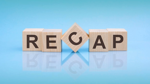 Слово RECAP написано на деревянных кубиках на ярко-синем фоне крупным планом деревянных элементов