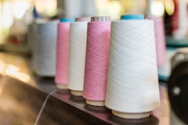 Receding line of alternating reels of pink and white cashmere yarn in a knitwear factory with selective focus to a pink spool