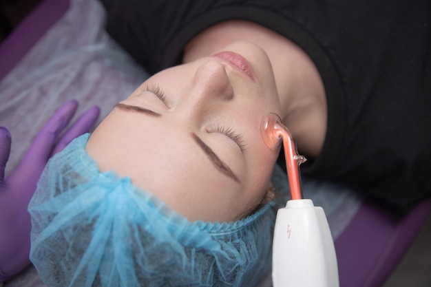 Receiving electric darsonval facial massage procedure at salon